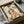 May include: Framed artwork showing a Japanese woman in flowing kimono with red, green, and coral floral patterns, holding a decorative fan. The print has an aged, vintage appearance with weathered texture and dark spots. Black frame sits in wooden shipping box with brown paper padding on white fabric surface.