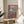 May include: Framed Japanese ukiyo-e style poster featuring a geisha in colorful kimono sitting on wooden deck, with Mount Fuji and cloudy sky in background, displayed on round wooden side table next to beige upholstered chair and houseplant in bright sunlit room with white walls