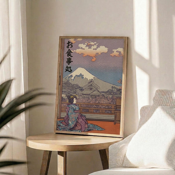 May include: Framed Japanese ukiyo-e style poster featuring a geisha in colorful kimono sitting on wooden deck, with Mount Fuji and cloudy sky in background, displayed on round wooden side table next to beige upholstered chair and houseplant in bright sunlit room with white walls