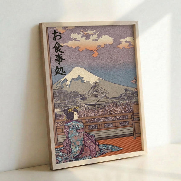 Traditional Japanese ukiyo-e style artwork in a light wooden frame showing a geisha in an ornate kimono with intricate patterns in blues, purples, and oranges. She kneels on a wooden terrace overlooking Mount Fuji in the distance, with traditional architecture and cloudy sky above. Japanese characters appear in the upper left corner. The framed print leans against a white wall.