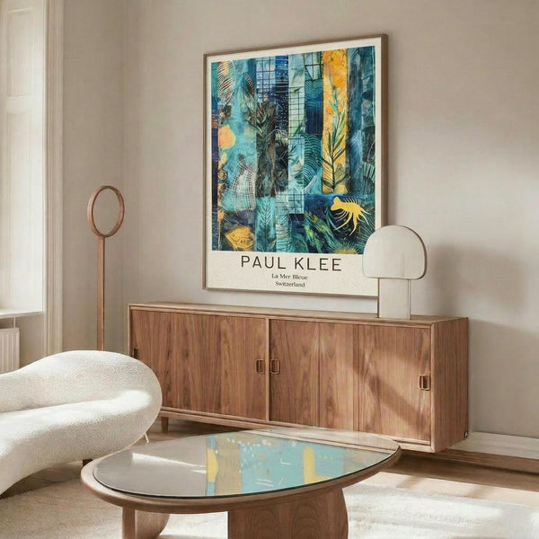 May include: A framed art print featuring an abstract tropical composition with blue, teal, yellow and green botanical elements including palm fronds and geometric patterns. The poster hangs above a mid-century modern walnut credenza with brass hardware. A white curved chair sits beside an oval glass-top coffee table with wooden base, and a brass floor lamp with white shade stands nearby. The room has cream walls and natural lighting.