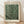 May include: Framed poster print with light wood frame leaning against white wall on wooden floor. Features green background covered in white polka dots of varying sizes creating optical illusion pattern. Text reads "YAYOI KUSAMA" at top, "1984" and "Modern Art" at bottom on cream colored border.
