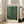 May include: Framed art print with green background covered in white dots of varying sizes, text reading "YAYOI KUSAMA" at top and "Modern Art 1984" at bottom, displayed on light wood floor against white wall next to beige upholstered chair in bright room with large windows