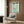 May include: Framed vintage Japanese flamingo poster with pink bird on turquoise background, displayed above modern cream armchair with geometric pillow in contemporary living room with wood paneled walls, brass floor lamp, and dark round side table with open book.