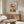 May include: Colorful mid-century modern botanical poster print displayed above wooden credenza in bright living room. White curved chair and glass coffee table in foreground. Artwork features stylized flowers in vibrant reds, yellows, blues and greens with geometric patterns. Natural wood furniture and neutral walls create Scandinavian-inspired interior setting.