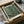 May include: Framed art print featuring green background with scattered white dots in varying sizes, displayed in light wood frame. Print shows "YAYOI KUSAMA" at top, "1984" in corner, and "Modern Art" at bottom. Artwork sits in cardboard shipping box with protective tissue paper and wooden packaging materials visible around frame.