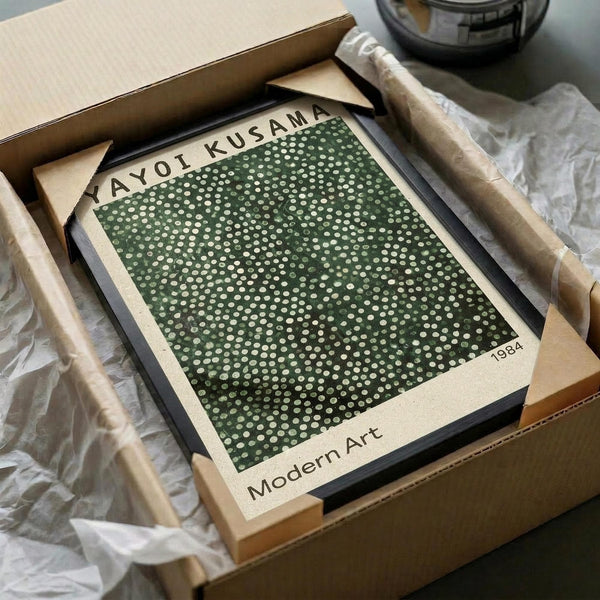 May include: Framed art print featuring green background with scattered white dots in varying sizes, displayed in light wood frame. Print shows "YAYOI KUSAMA" at top, "1984" in corner, and "Modern Art" at bottom. Artwork sits in cardboard shipping box with protective tissue paper and wooden packaging materials visible around frame.