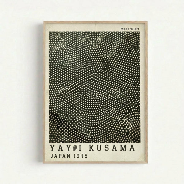 Framed art print featuring a black square filled with white polka dots of varying sizes creating a dense, textured pattern. The dots appear more concentrated in the center and gradually become sparser toward the edges. Below the dotted square is text reading "YAYOI KUSAMA" and "JAPAN 1945" in bold black letters on cream-colored paper. The print is displayed in a light wood frame against a white wall, with "modern art" text visible in the upper right corner.