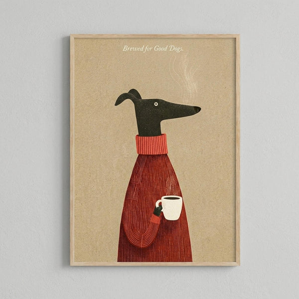 Minimalist illustration of a black greyhound wearing a red ribbed sweater, holding a white coffee mug with steam rising above. The dog is shown in profile against a tan textured background with "Brewed for Good Dogs" text at the top. The artwork is displayed in a light wood frame hanging on a white wall.