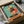 May include: Framed poster print being unboxed from brown cardboard packaging with white tissue paper. The artwork shows a stylized rooster wearing black polka dot clothing and sunglasses, positioned behind an orange turntable with black vinyl record. Features retro mid-century modern illustration style with teal background and coral red circular accent. Black frame visible, approximately 12x12 inches based on packaging size.
