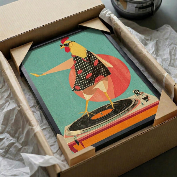May include: Framed poster print being unboxed from brown cardboard packaging with white tissue paper. The artwork shows a stylized rooster wearing black polka dot clothing and sunglasses, positioned behind an orange turntable with black vinyl record. Features retro mid-century modern illustration style with teal background and coral red circular accent. Black frame visible, approximately 12x12 inches based on packaging size.
