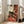 May include: Large framed art print leaning against white wall in bright modern living room with beige sofa and windows. Artwork shows woman with elongated face and brown hair bun, wearing black top and coral red skirt, seated in chair. Painting features Modigliani's distinctive style with muted earth tones and simplified forms. Print has thin light wood frame and appears oversized compared to furniture.