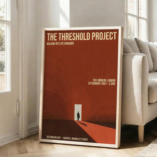 May include: A framed minimalist art poster with rust-red background displayed in a bright living room corner. The poster shows a silhouetted figure standing before a white doorway or opening, with geometric shapes and typography. The wooden frame leans against white walls near tall windows, positioned next to a beige upholstered chair. Natural sunlight streams across the wooden floor, creating shadows and highlighting the poster's warm earth tones and clean modern design.