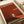 May include: A minimalist art poster with rust-red gradient background featuring a small silhouetted figure standing in a white doorway opening. The print displays white text reading "THE THRESHOLD PROJECT" and "WALKING INTO THE UNKNOWN" along with exhibition details for Tate Modern London. The poster lies flat on white paper with rolled paper tubes visible in the composition, showing the artwork's clean geometric design and warm earth-toned color palette.