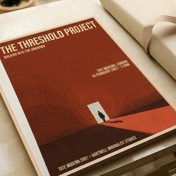 May include: A minimalist art poster with rust-red gradient background featuring a small silhouetted figure standing in a white doorway opening. The print displays white text reading "THE THRESHOLD PROJECT" and "WALKING INTO THE UNKNOWN" along with exhibition details for Tate Modern London. The poster lies flat on white paper with rolled paper tubes visible in the composition, showing the artwork's clean geometric design and warm earth-toned color palette.