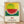May include: Framed poster print leaning against white wall on light wood floor. Artwork features vibrant dotted watermelon slice with green striped rind against yellow speckled background and blue-green landscape. Below image are red Japanese characters and English text about courage. Natural wood frame with white mat border.