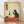 May include: Framed vintage-style Japanese ukiyo-e artwork showing a black cat sitting on a red tablecloth, holding a wine glass. The scene includes a wine bottle, grapes, and cheese on the table. Features aged beige background with orange Japanese text cartouche in upper left. Light wood frame displayed against white wall on wooden floor with natural lighting.