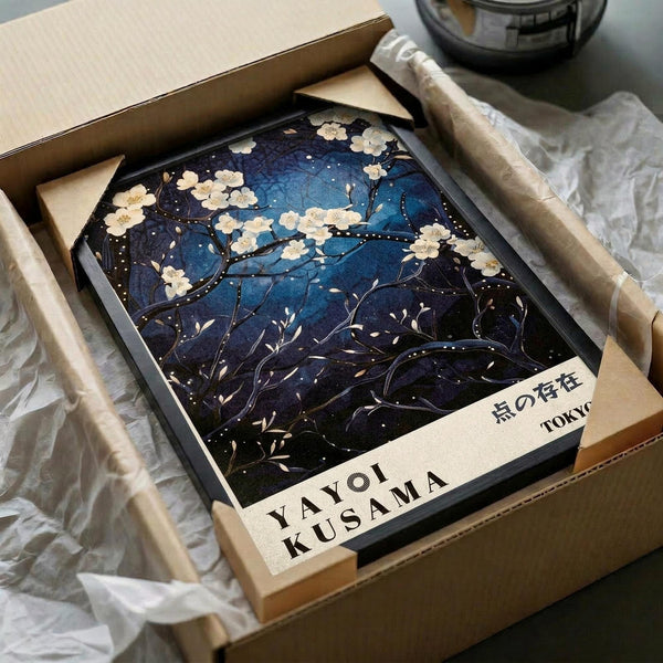 May include: Framed art print featuring cherry blossom branches with white flowers against a deep blue starry night sky, displayed in black frame within cardboard packaging surrounded by brown paper wrapping materials on white fabric surface