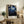May include: Framed poster with deep blue night scene featuring white cherry blossoms on dark branches against starry sky, displayed on rustic wooden console table beside cream armchair, fern plant, ceramic vases and stacked books in neutral-toned living room setting