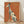May include: Framed poster print leaning against white wall on light wood floor. Orange textured background features stylized greyhound illustration in cream and teal colors with spotted pattern. French text "L'élégance ne vieillit pas" in golden script lettering. Natural wood frame, soft window light casting shadows on wall.