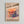 May include: Framed poster on white wall featuring a tall stack of colorful pancakes with syrup dripping down. The artwork has a pink background with Japanese text and "Pancake Paradise: Stack Your Happiness! Fluffy, Golden, and Irresistible" at top, "itadakimasu" at bottom. Light wood frame against textured white wall.