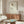 May include: Framed minimalist line drawing of a rose with colorful geometric petals in red, yellow, and green on cream background, displayed above wooden sideboard in modern living room with white curved chair, glass coffee table, and warm natural lighting