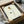 May include: Minimalist line art poster featuring geometric shapes in red, yellow, and green forming an abstract floral design with thin black stems, displayed in a black frame being unpacked from cardboard shipping box with protective tissue paper and wooden frame corners visible