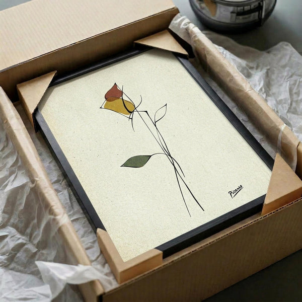 May include: Minimalist line art poster featuring geometric shapes in red, yellow, and green forming an abstract floral design with thin black stems, displayed in a black frame being unpacked from cardboard shipping box with protective tissue paper and wooden frame corners visible