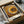 May include: Framed poster with concentric circles in warm earth tones - yellows, oranges, browns, and creams - created from dotted patterns radiating from center. Japanese text visible at bottom. Print sits in cardboard shipping box with protective tissue paper, surrounded by brown paper wrapping materials on white surface.