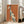 May include: Framed poster with orange background featuring stylized greyhound illustration in teal and cream colors, with French text "L'elegance NE VIEILLIT PAS" in golden lettering. White frame leaning against white wall next to beige upholstered chair in bright, modern living room with large windows and natural lighting.