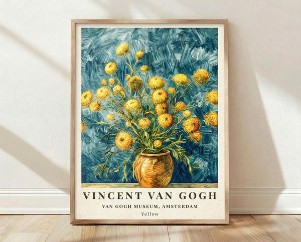 May include: Framed poster print displaying Van Gogh's painting of yellow wildflowers in a brown ceramic vase against a swirling blue background, featuring museum exhibition text below the artwork. The light wood frame leans against a white wall on wooden flooring with natural shadows cast across the scene.