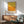 May include: Abstract art print with yellow and orange color field design in wooden frame, displayed above modern walnut credenza with ceramic table lamp, next to mid-century modern teal upholstered armchair with wooden arms in bright living room with natural sunlight casting shadows on white wall