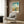 May include: Vintage Georgia travel poster featuring Savannah's historic district with colonial buildings, church spires, and blue sky with white clouds. Displayed in white frame on wood-paneled wall above cream upholstered chair with geometric pillow. Modern brass floor lamp and dark side table with open book complete the styled room setting.