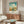 May include: Vintage Georgia travel poster featuring Savannah Historic District with blue sky and white clouds, displayed in thin wooden frame above mid-century modern walnut credenza. Room shows white upholstered chair, oval glass coffee table, and minimalist white table lamp in bright, clean interior setting.