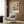 May include: Framed botanical art print featuring large flowers in cream, orange, and pink tones with detailed leaves on dark green background, displayed above beige upholstered chair with geometric pillow in modern living room with wood paneled walls and brass floor lamp