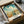 May include: Vintage-style travel poster of Georgia featuring Savannah Historic District with colonial buildings, Spanish moss-draped trees, and cloudy blue sky, displayed in black frame inside cardboard shipping box with protective tissue paper wrapping