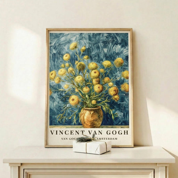 May include: Framed Van Gogh poster print featuring yellow chrysanthemum flowers in a brown vase against swirling blue brushstroke background, displayed on light wood console table with small white gift box, neutral wall backdrop, natural lighting creating soft shadows