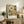 May include: Framed botanical art print featuring large detailed flowers in cream, orange and green tones with dotted patterns, displayed on rustic wooden sideboard next to fern plant, ceramic vases, and stacked books in neutral-toned living room setting
