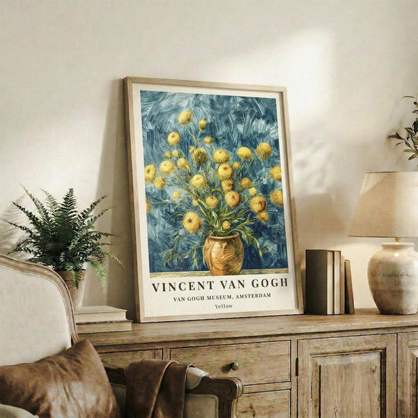 May include: Framed Van Gogh museum poster featuring yellow spherical flowers in brown vase against swirling blue background, displayed on rustic wooden sideboard alongside fern plant, ceramic vase, and books in neutral-toned living room with beige armchair and white walls