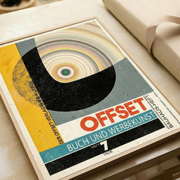 May include: Vintage 1926 Bauhaus poster print displayed flat on white surface next to rolled cream paper tube. Design features bold geometric composition with large black semicircle containing concentric rings in cream, yellow, and orange tones with green center dot. German text "OFFSET" in red letters and "BUCH UND WERBEKUNST" in white on teal band. Yellow section on left with black German text. Speckled texture throughout design gives aged appearance.