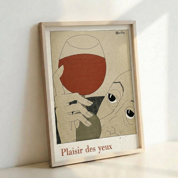 May include: Framed art print leaning against white wall showing abstract illustration with hands holding wine glass filled with red liquid, stylized eyes, and French text "Plaisir des yeux" at bottom. Artwork features muted beige, terracotta, and olive green colors in minimalist style within light wood frame.