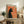 May include: Framed vintage-style poster featuring a black cat silhouette smoking a cigarette against an orange background, displayed on a rustic wooden sideboard alongside books, ceramic vases, and a potted fern in a cozy living room setting with neutral walls and upholstered furniture.
