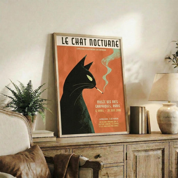May include: Framed vintage-style poster featuring a black cat silhouette smoking a cigarette against an orange background, displayed on a rustic wooden sideboard alongside books, ceramic vases, and a potted fern in a cozy living room setting with neutral walls and upholstered furniture.