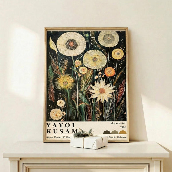 May include: Framed botanical art print with intricate illustrated flowers and seed pods in cream, yellow, and orange tones against a dark background, displayed on a light wood console table with a small wrapped gift box beside it on a neutral wall.