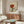 May include: Framed vintage-style art poster showing hands holding a wine glass filled with red wine, featuring stylized eyes and "Plaisir des yeux" text at bottom. Displayed above a mid-century modern walnut credenza with white mushroom table lamp, alongside a white curved chair and oval glass coffee table in a minimalist living room with cream walls.