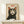 May include: A framed poster featuring a black and white tuxedo cat with large golden eyes and pink inner ears against a cream background, with red "Meow" text above. The artwork shows detailed whiskers and fur texture in a vintage illustration style. The wooden frame sits on a light wood shelf next to a small white wrapped gift box against a white wall.
