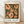 May include: Framed art print leaning against white wall on light wood floor. The poster features abstract figures in peachy-orange tones against dark gridded background, reminiscent of mid-century modern style. Simple wooden frame with white matting. Natural lighting creates soft shadows on textured white wall behind the artwork.