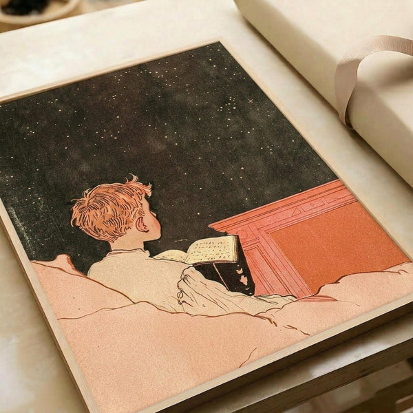 May include: Vintage-style art print showing a person with reddish hair reading in bed under a starry night sky. The illustration features warm coral and pink tones contrasting with a dark starlit background. The print appears mounted or framed, displayed alongside white paper materials and a cream ribbon on a neutral surface.