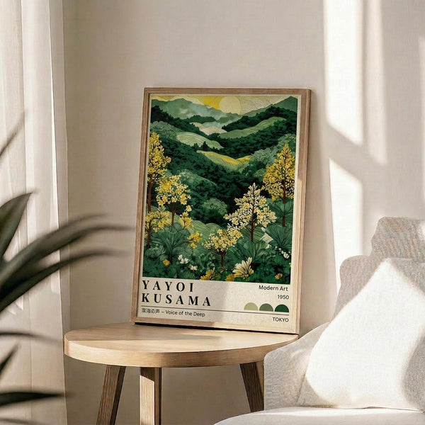 May include: Framed art poster displaying a lush green landscape with rolling hills, yellow flowering trees, and a pale sun in a golden sky. The artwork features Japanese text and "Modern Art 1950 Tokyo" at the bottom. The wooden-framed print sits on a round wooden side table next to a beige upholstered chair, with natural sunlight casting shadows across white walls and a plant visible in the corner.