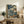 May include: Japanese woodblock print artwork in wooden frame showing dramatic blue swirling waves and clouds with a wooden bridge and small figure, displayed on rustic wood console table alongside potted fern, books, and ceramic vessels in neutral-toned living room setting